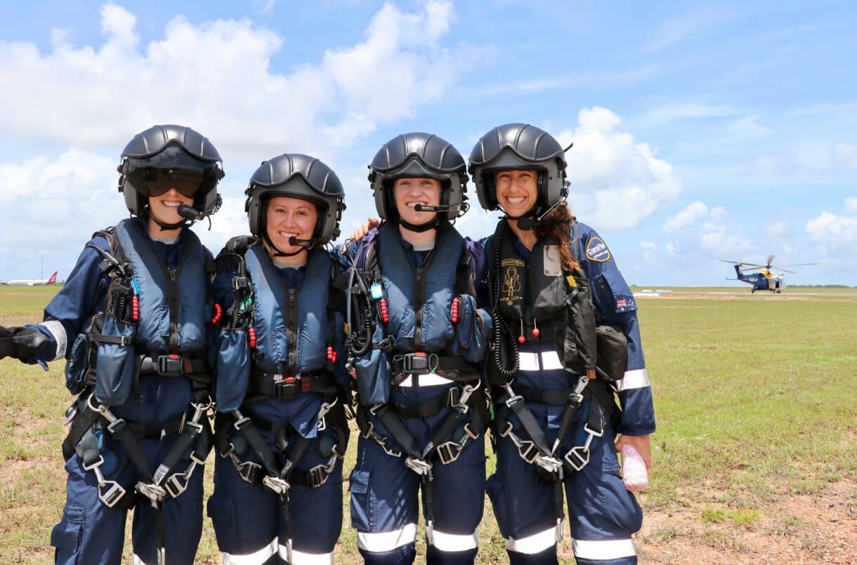 Four women on a field with helicopter in the background